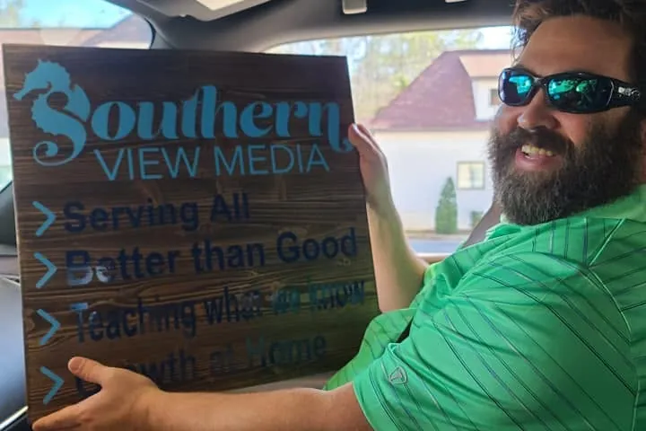 Southern View Media team member holds a wooden sign listing the company values
